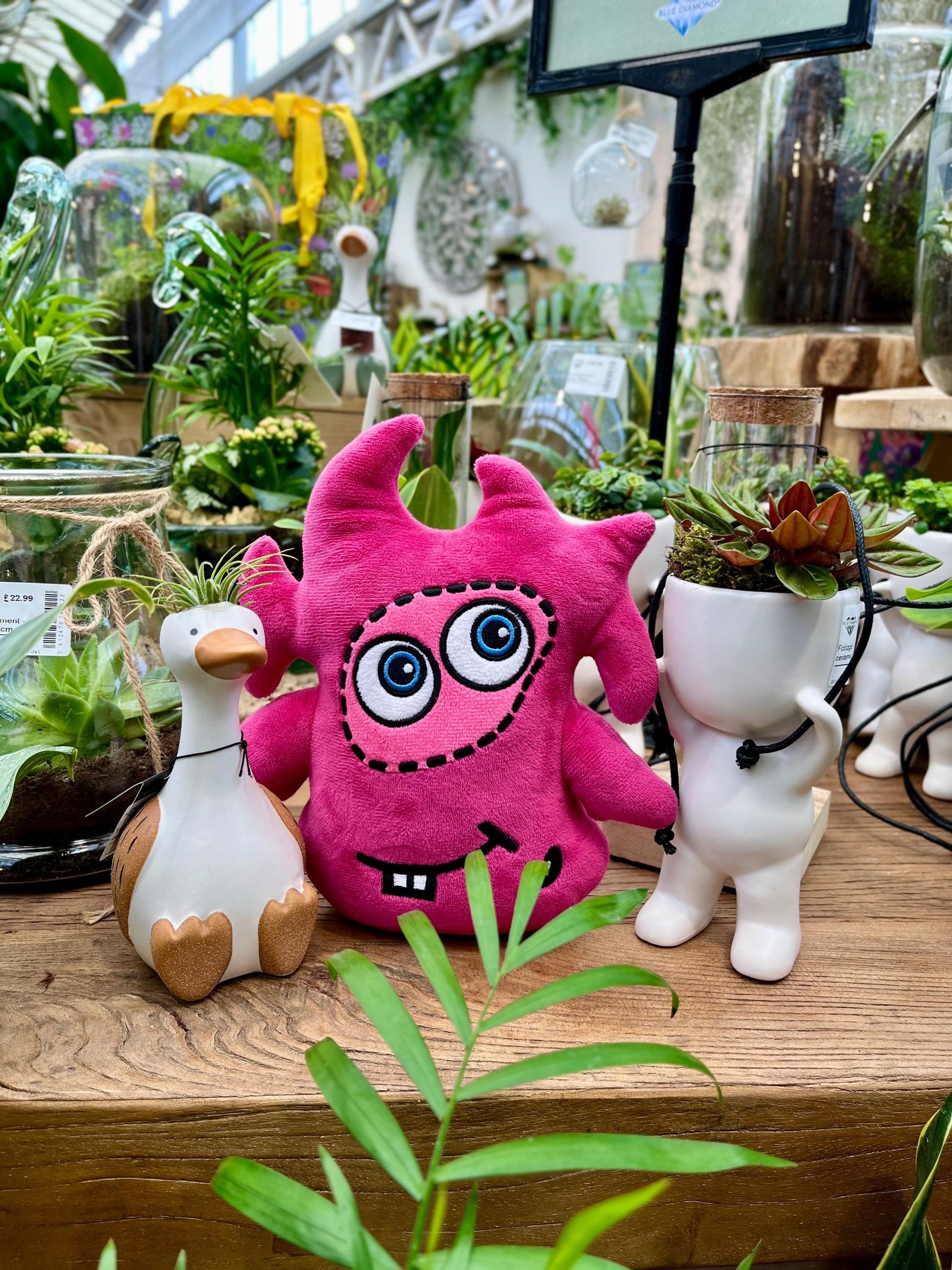 CwaZyBean Aliens Lagion Pink  award winning plush toy with googly eyes on a wooden surface surrounded by plants